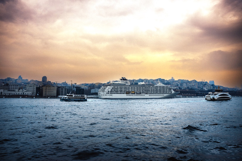 Kreuzfahrtschiff fährt bei Sonnenuntergang vor einer Küstenstadt Kreuzfahrtschiff fährt bei Sonnenuntergang vor einer Küstenstadt